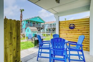 Un espace extérieur abrité, avec des chaises Adirondack bleues, un barbecue et une clôture en bois.