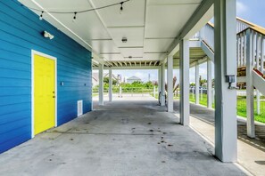 Ein überdachter Außenbereich mit blauer Wand und gelber Tür, einem Betonboden und Blick auf eine Wohngegend im Hintergrund.