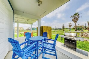 Une terrasse couverte avec des fauteuils Adirondack bleus, une table ronde et un barbecue.