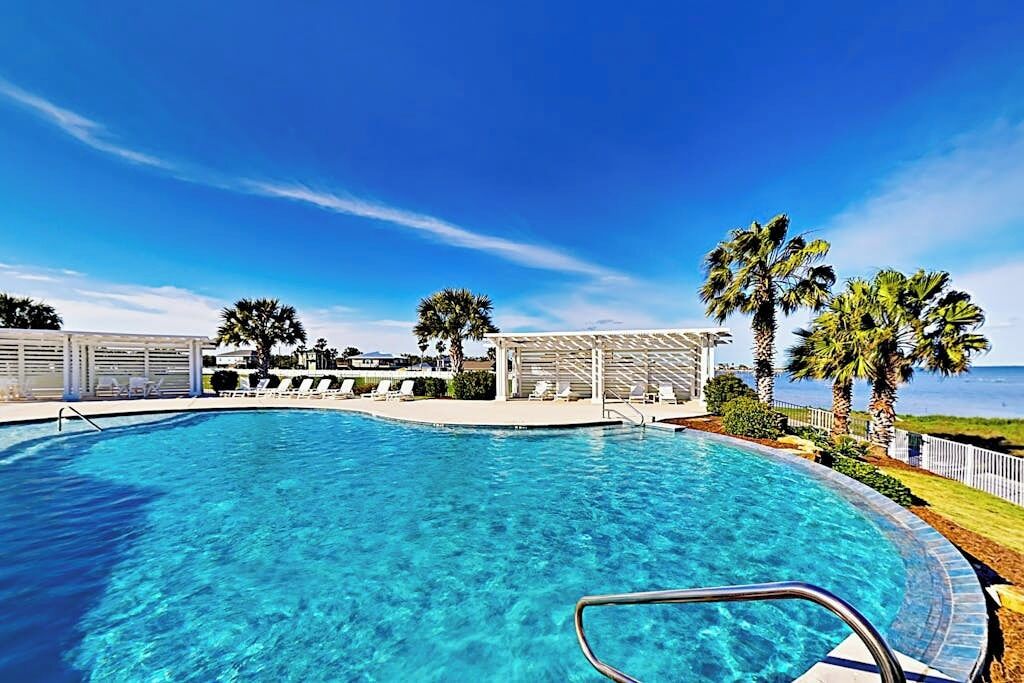 A clear blue pool with a poolside area, palm trees, and a view of the ocean.