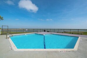 A rectangular swimming pool with a clear blue water, surrounded by a concrete deck and a metal fence. - Baydreaming - Bay Views, Pool & Boat Slip (Rockport)