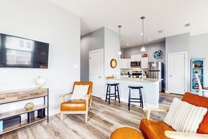 Ein modernes Wohnzimmer mit einer Couch, einem Sessel, einem Couchtisch und einem an der Wand montierten Fernseher.