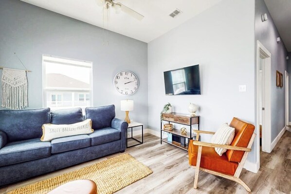A living room with a blue sofa, a wooden coffee table, a clock on the wall, and a television mounted on the wall. - Hook Line and Sleeper (Rockport)