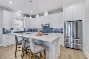 A modern kitchen with white cabinets, a stainless steel refrigerator, and a central island with bar stools. - Palm Breeze at the Reserve (Rockport)