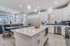 A modern kitchen with white cabinetry, a central island, and pendant lighting. - Palm Breeze at the Reserve (Rockport)