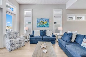 A living room with a blue sofa, a patterned armchair, and a coffee table with a starfish decoration. There is a painting of a sea turtle on the wall. - Palm Breeze at the Reserve (Rockport)