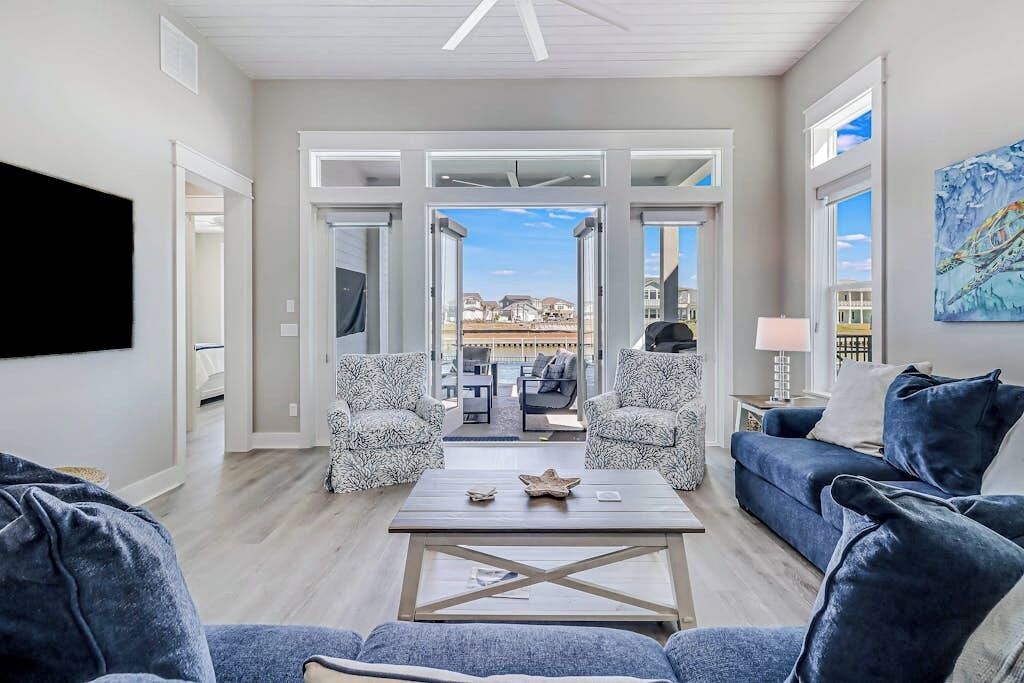 A spacious living room with a large window, two patterned armchairs, a blue sofa, and a coffee table with decorative items.