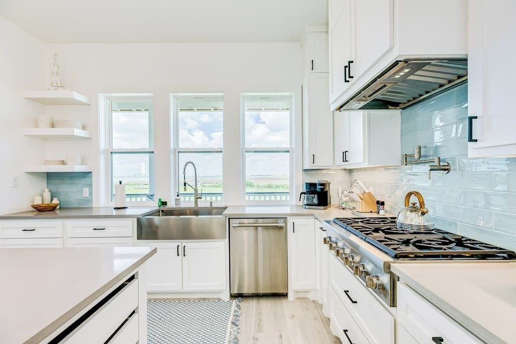 A modern kitchen with white cabinetry, a stainless steel sink, a dishwasher, and a gas stove.