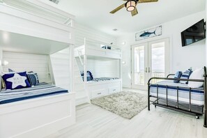 Ein Zimmer mit Etagenbetten, Deckenventilator, Fernseher und einer Tür, die auf einen Balkon führt.