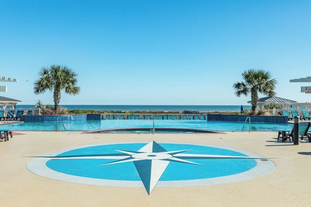 A pool area with a compass design, palm trees, and a view of the ocean.