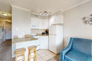 A compact kitchen with white cabinets, a granite countertop, and a blue chair. - Casa Del Mar - The Seaside (Galveston)