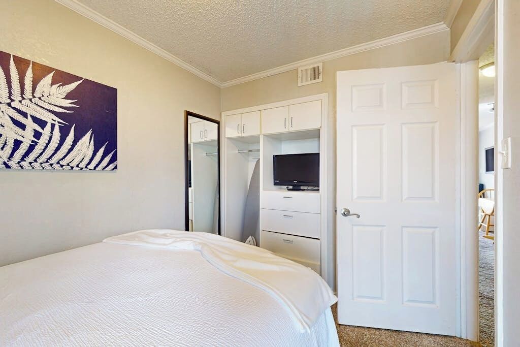 A bedroom with a bed, a television on a stand, a wardrobe, and a door.
