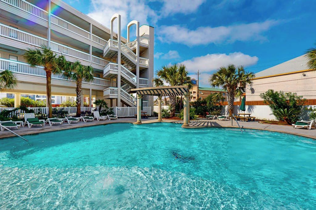 A hotel with a pool, multiple balconies, and palm trees.