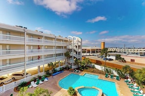 A multi-story hotel with a pool area, outdoor seating, and a clear sky. - Casa Del Mar - The Seaside (Galveston)