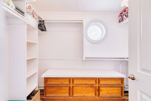 Ein weißer Kleiderschrank mit Holoszieren, einem weißen Regal und einem runden Spiegel an der Wand.