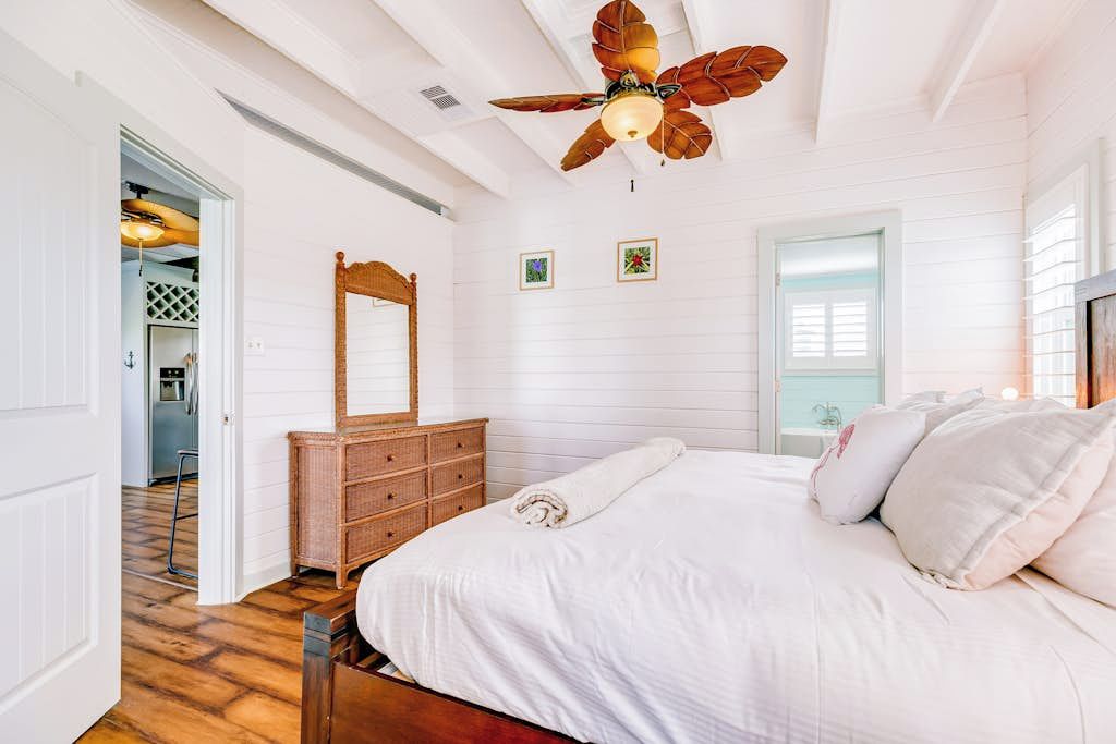 Un dormitorio con una cama grande, un ventilador de techo, un aparador y una puerta que da a otra habitación.