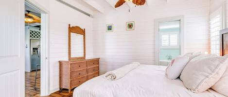 Un dormitorio con una cama grande, un ventilador de techo, un aparador y una puerta que da a otra habitación.