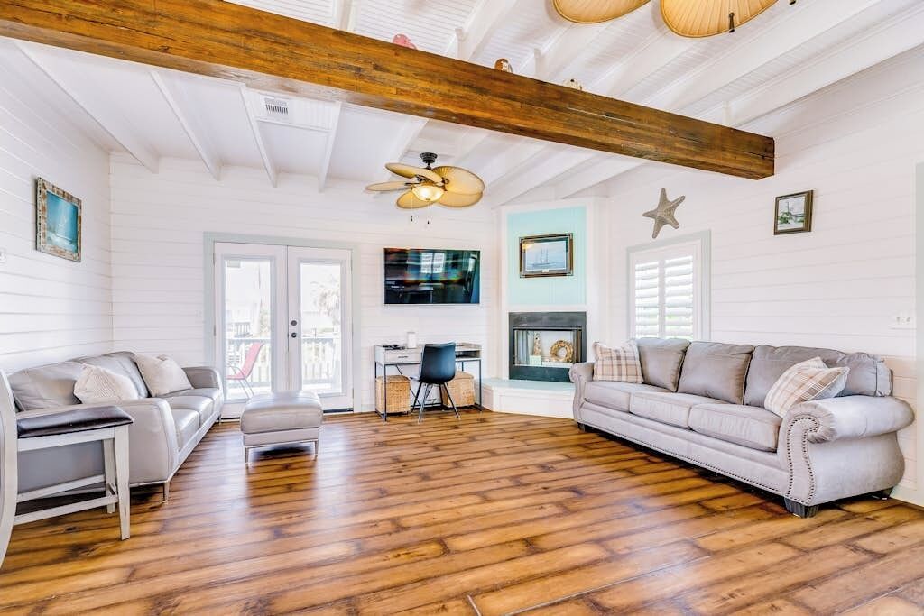 Un salon spacieux doté d’un plancher en bois, de deux canapés, d’une table basse, d’un ventilateur de plafond et d’une cheminée.