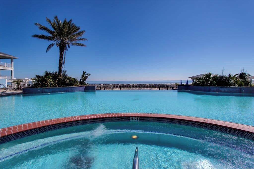 Ein Pool mit freiem Blick auf den Ozean, umgeben von Palmen und Liegestühlen.