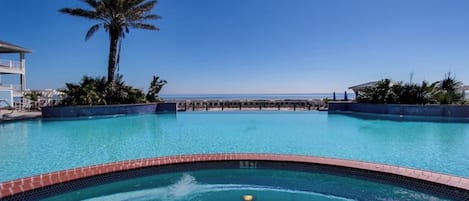 Una piscina con vistas despejadas al océano, rodeada de palmeras y sillas de descanso.