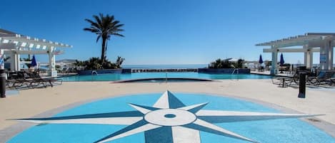 A pool area with a large compass design, lounge chairs, and a palm tree.
