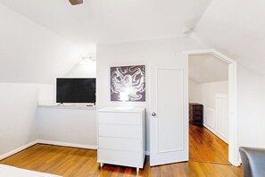 A room with a white dresser, a television on a shelf, and a door leading to another room. - Central Galveston Cottage (Galveston)