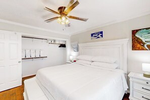 Ein Hotelzimmer mit einem Bett, einem Deckenventilator, einem Nachttisch, einem an der Wand befestigten Schild und einem Gemälde.