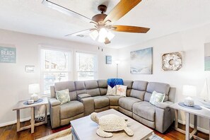 A living room with a sectional sofa, a ceiling fan, and a turtle decoration. - Central Galveston Cottage (Galveston)