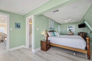 Ein Schlafzimmer mit einem Bett, Nachttischen, einem Deckenventilator, Kunstwerken und einem Fernseher.