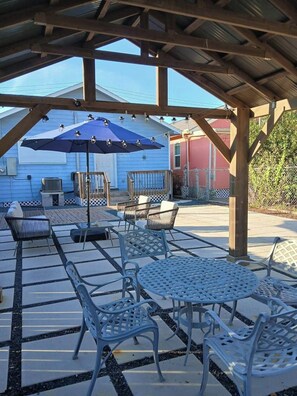 Eine Außenpatio mit Metalltischen und -stühlen, einem blauen Sonnenschirm und einer Holzpergola.