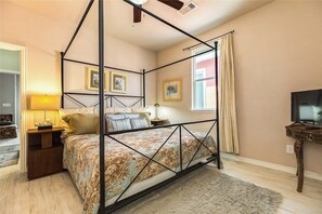 A four-poster bed with a floral bedspread, bedside tables, a television, and framed pictures on the walls. - Bella Vie - Fenced Yard, Walk to the Beach (Galveston)