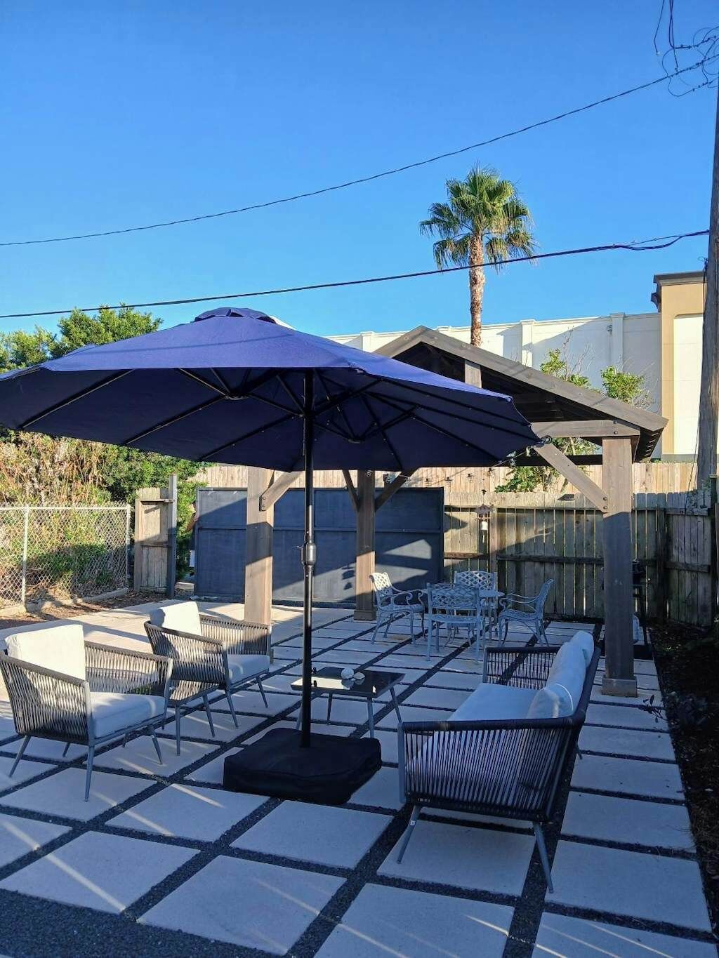 Un espace patio aménagé avec du mobilier d’extérieur, notamment des chaises et une table, placé sous un grand parasol.