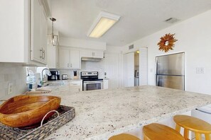 Eine moderne Küche mit weißen Schränken, einer Arbeitsplatte aus Granit, einer Holzschüssel und einem Edelstahlkühlschrank.