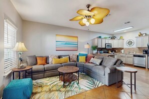 Ein modernes Wohnzimmer mit einem Ecksofa, einem runden Couchtisch und einer Küche im Hintergrund.
