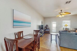 Ein Essbereich mit einem Holztisch, Stühlen, einem Fernseher und einer Couch im Hintergrund.