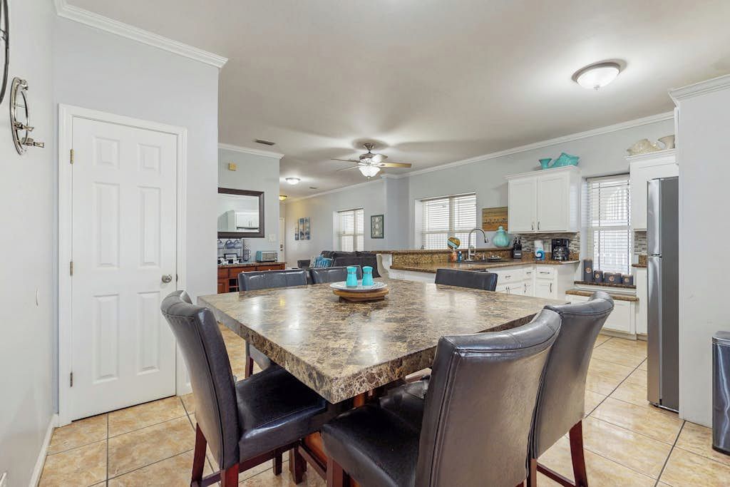 A spacious kitchen with a granite countertop, white cabinets, and a dining area with a marble table and leather chairs.