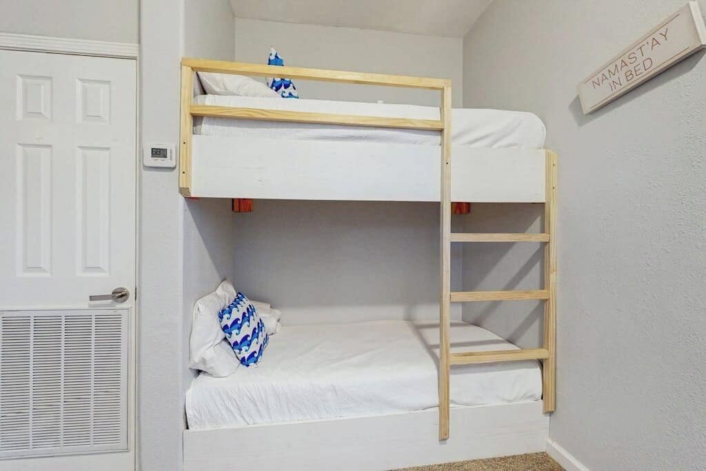 Una litera con una escalera, una puerta blanca y un letrero en la pared.