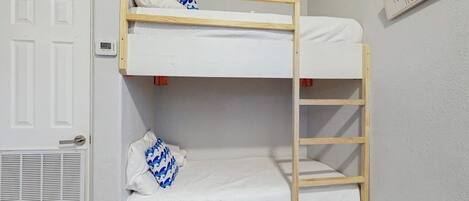 Una litera con una escalera, una puerta blanca y un letrero en la pared.