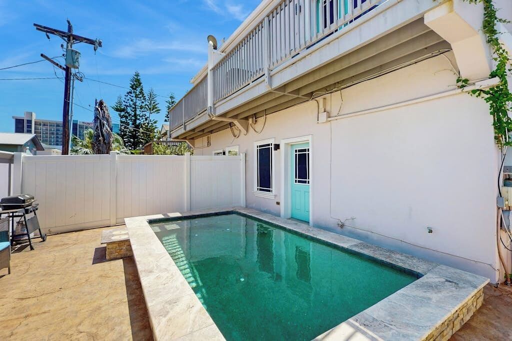 Piscina residencial com cerca branca, porta e varanda.