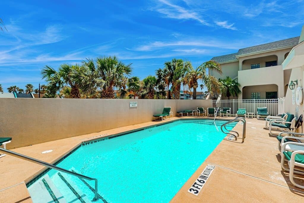 A swimming pool with a clear blue water, surrounded by lounge chairs and palm trees.