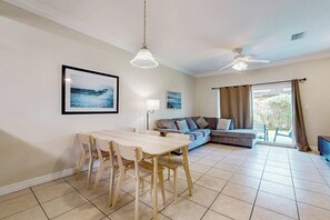 Ein Wohnzimmer mit Esstisch, Sofa, Deckenventilator und großem Fenster mit Vorhängen.
