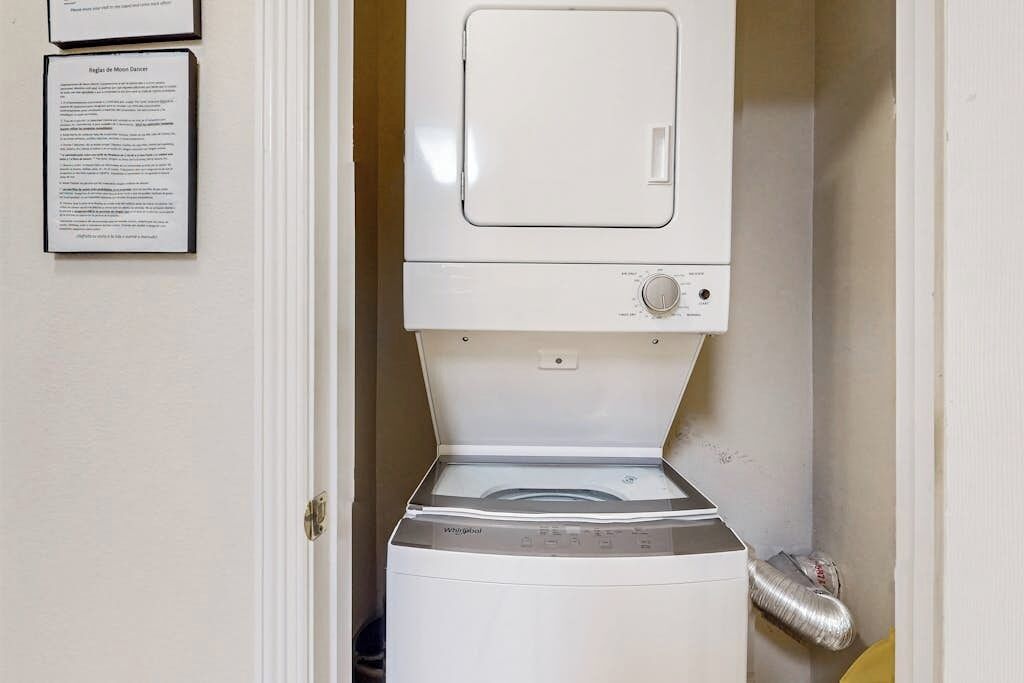 Máquina de lavar e secar compacta numa lavanderia pequena, com porta e tubo de ventilação.