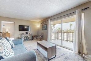 A living room with a sofa, a coffee table, a TV, and a balcony with a view. - Marlin Arms Condominiums #9 (South Padre Island)