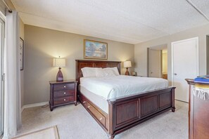A bedroom with a large bed, two bedside tables with lamps, a dresser, and a door leading to another room. - Marlin Arms Condominiums #9 (South Padre Island)