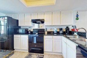 A kitchen with white cabinetry, a black refrigerator, a stove, and a microwave. - Suntide II Condominiums #507 (South Padre Island)