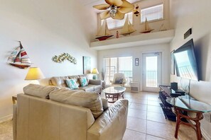 A spacious living area with a sofa, coffee table, and a television. There are decorative sailboats and a ceiling fan. - Suntide II Condominiums #507 (South Padre Island)