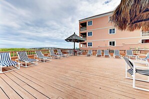 Une terrasse dotée de chaises longues et d’un parasol en chaume, offrant une vue sur un immeuble avec des balcons.