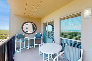 A balcony with a round mirror, two chairs, a table, and a view of the ocean. - Suntide II Condominiums #207 (South Padre Island)