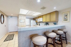 A kitchen with a bar area, wooden cabinets, a microwave, and a window with blinds. - Suntide II Condominiums #207 (South Padre Island)