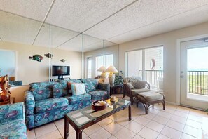 A living room with a sofa, armchair, and a coffee table. There is a television and a window with blinds. - Suntide II Condominiums #207 (South Padre Island)